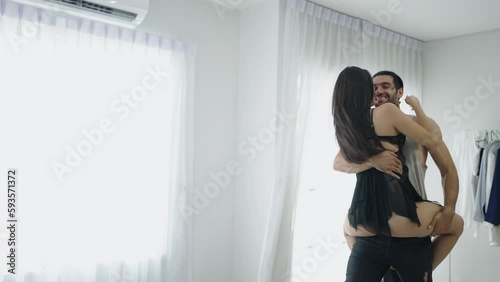 Romantic sexy moments lifestyle for a young couple at home, hot Asian lady wearing black bra teasing young aroused man on bed, passionate couple enjoying sensual foreplay petting before making love