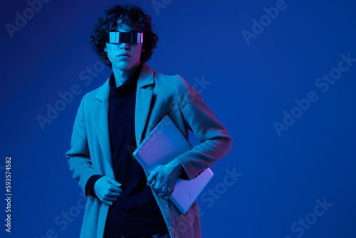 A man with a laptop in his hands and a jacket, futuristic glasses in blue light, Blue Perennial color, cyber security, technology, laptop copy space, template, trendy neon, freelance work, hacker
