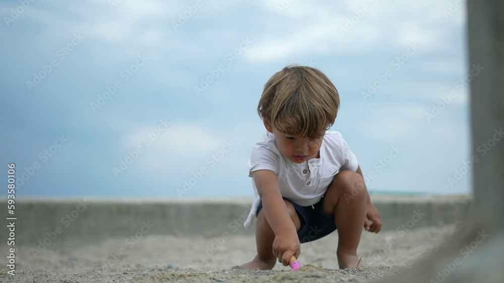 Child throwing sand in the air with shovel. One small boy playing at sandbox during sunny day. Playful kid having fun outdoors. Childhood lifestyle