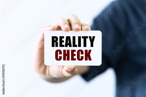 Reality check text on blank business card being held by a woman's hand with blurred background. Business concept about reality check.