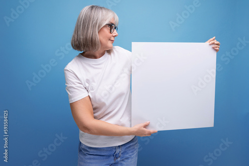 mature woman with gray hair holding blank billboard with mocap on studio background