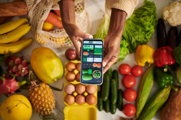 Woman holding smartphone with food delivery application over table with fresh groceries