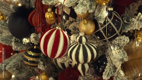 Christmas tree decorated with artificial snow, shining lights, golden feathers, multicolor Christmas tree toys and balls with glitter. Winter holidays with family and presents in a cozy home. 