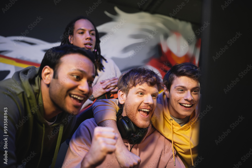 Obraz premium Excited multiethnic gamers looking at computer monitor in gaming club.