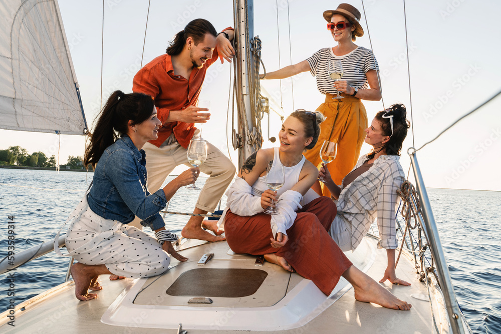 Group of happy friends drinking wine and relaxing on the sailboat during sailing in sea Group of happy friends drinking wine and relaxing on the sailboat during sailing in sea