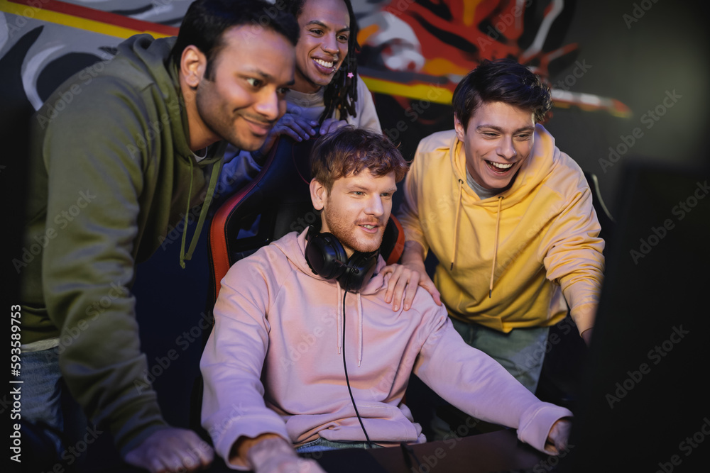 Fototapeta premium Multiethnic friends standing near friend playing computer game in cyber club.