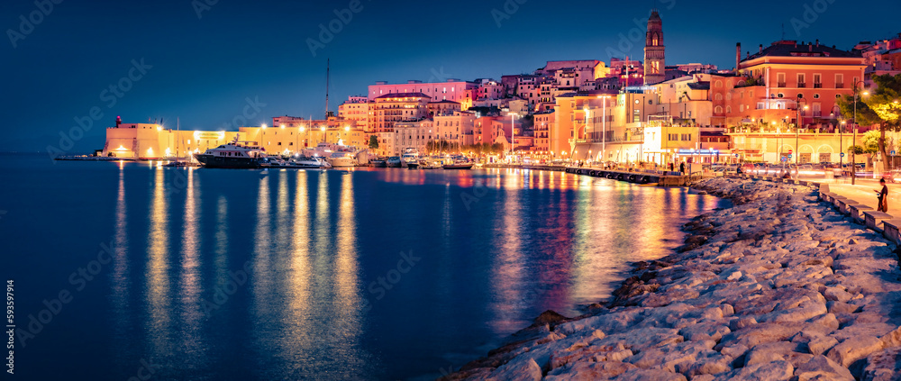Illuminated quay in Gaeta town with Cathedral Basilica of Gaeta church on background. Panoramic evening view of coast of Mediterranean sea, Italy, Europe. Traveling concept background.