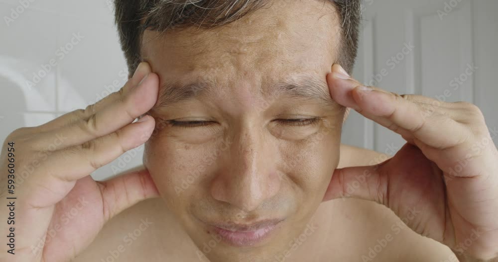 Depressed Asian man with headache and hangover in bathroom in morning rubs his face. Portrait of sick guy with flu, cold looking at camera as at mirror. Midlife crisis, depression and stress. Depressed Asian man with headache and hangover in bathroom in morning rubs his face. Portrait of sick guy with flu, cold looking at camera as at mirror. Midlife crisis, depression and stress.