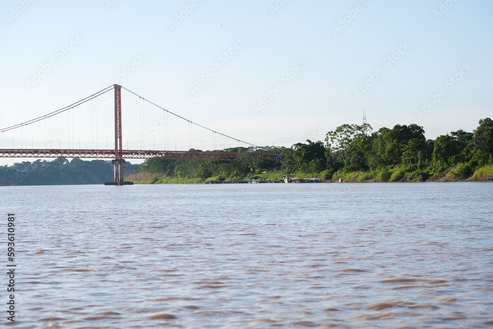 Fototapeta premium Puerto Maldonado Billinghurst red bridge with Amazon river, blue sky, forest background in Peru. Selective focus of river. Open space area. 