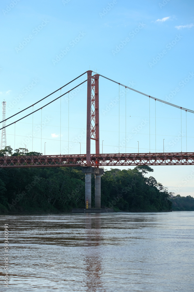 Puerto Maldonado Billinghurst red bridge with surface reflection on Amazon river, blue sky, forest background in Peru. Selective focus of river. Open space area. Puerto Maldonado Billinghurst red bridge with surface reflection on Amazon river, blue sky, forest background in Peru. Selective focus of river. Open space area.