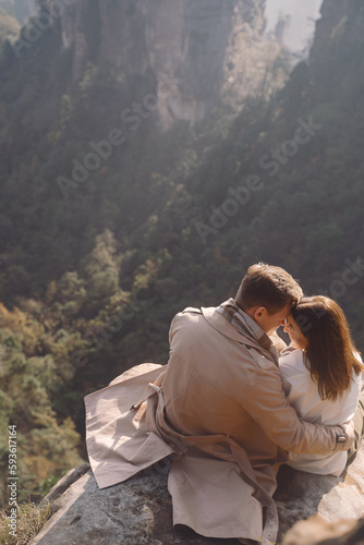 newly enageged couple hugging and holding hands as they are sitting on a rock at zhangjiajie national forest park