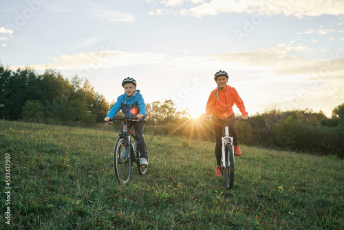 Mother and son ride a bike. Happy cute boy in helmet learn to riding a bike in park on green meadow at sunset time. Family weekend. 