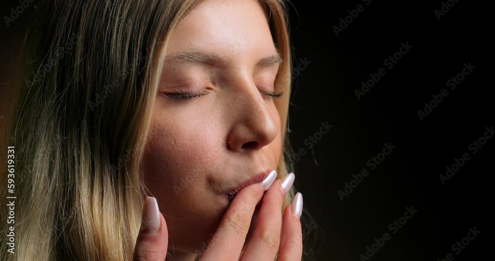 Close-up static shot of a beautiful blonde model licking her finger with pleasure against a black background Close-up static shot of a beautiful blonde model licking her finger with pleasure against a black background