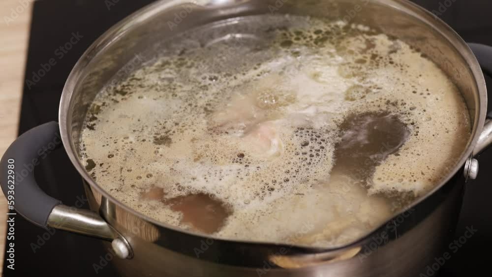 Close up video of hand mixing chicken meat broth water in stainless pan on cooker panel and defoam, remove foam from soup with spoon. Clean cook diet, low calories soup. High angle view, 4k resolution Close up video of hand mixing chicken meat broth water in stainless pan on cooker panel and defoam, remove foam from soup with spoon. Clean cook diet, low calories soup. High angle view, 4k resolution