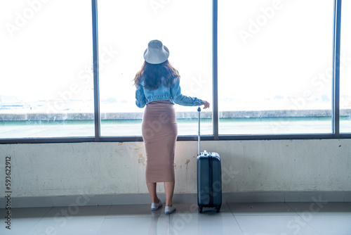 Asian female tourist backpacking in denim jacket dress dragging luggage, raising hands, cheering and greeting friends in airport terminal photo