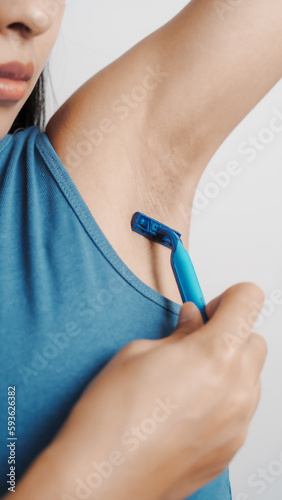 Use a razor  Young confident asian chinese female armpit with blue tank top isolated background.