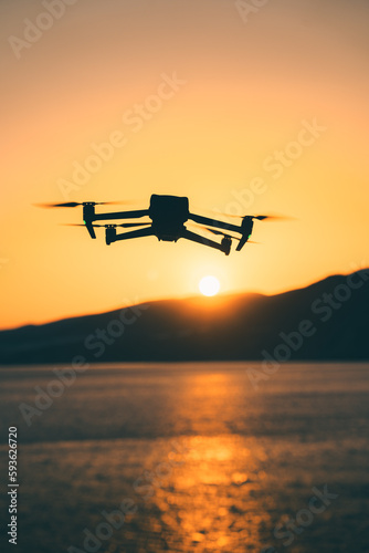 Silhouette of a quadcopter drone flying over the Mediterranean Sea during sunset in Crete, Greece