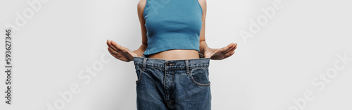 Young pretty asian chinese woman weight loss with oversize big blue jean pants, isolated background.