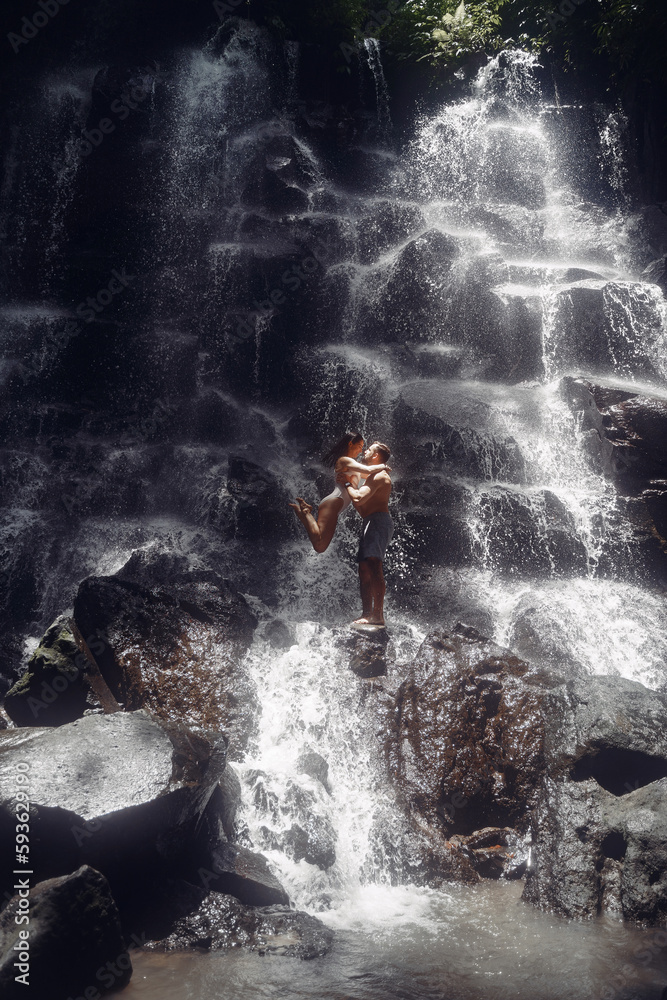 Obraz premium Couple stand under a large waterfall