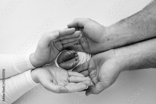 Children's leg in the hands of mother, father, parents. Feet of a tiny newborn close up. Little baby foot. Mom and her child. Happy family concept. Black and white photo of motherhood.