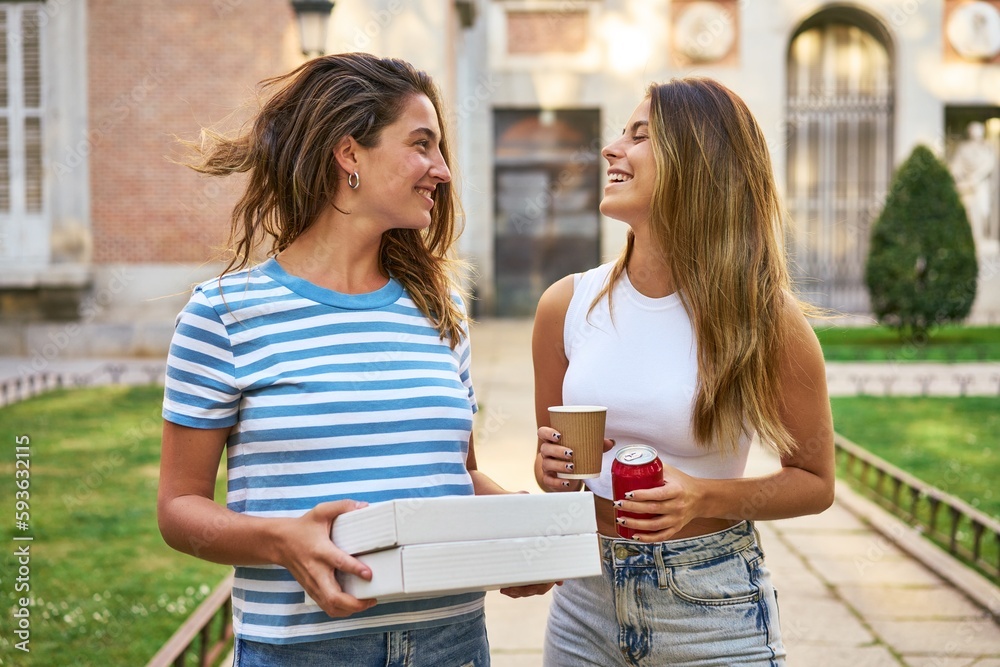 Two friends happily carrying pizzas through park towards home. Two friends happily carrying pizzas through park towards home.