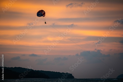 Distant shot of a paraglider with a parachute against the golden sky at sunset