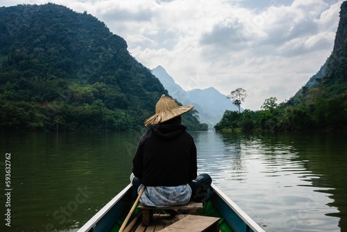 Asian boy with a straw hat on the riverboat on the Nam Ou River in the Mountains of Nong Khiaw