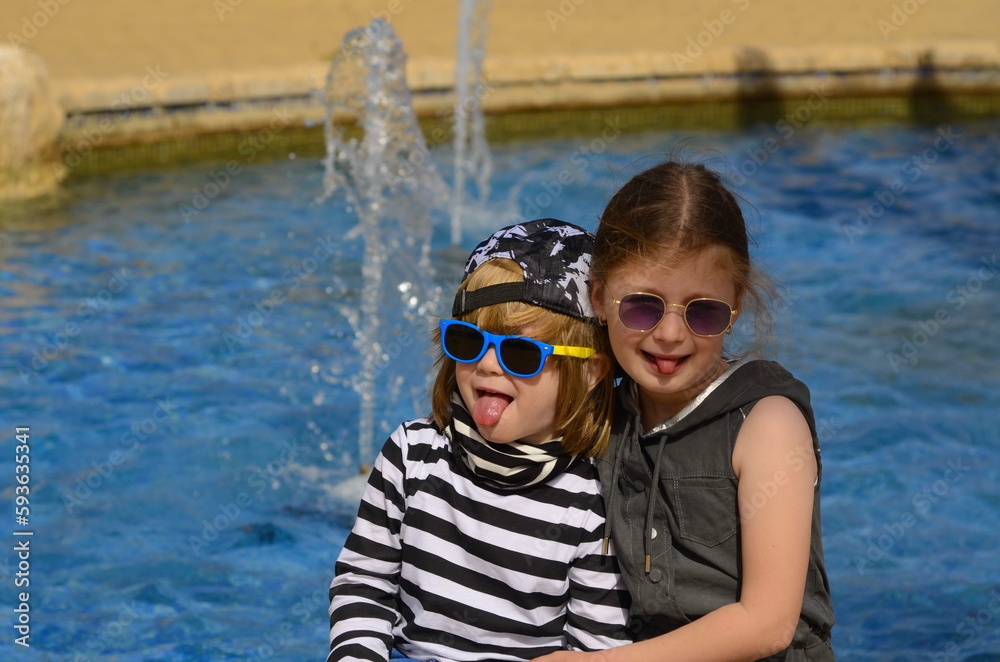 Children on the background of the pool, fountain. Little boy and girl in sunglasses. The girl hugs the boy, brother and sister, friends on vacation, vacation. family travel