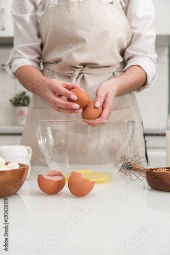 Woman hands are holding eggs for baking near the table with ingredients: flour, cottage, milk, nuts in light kitchen.