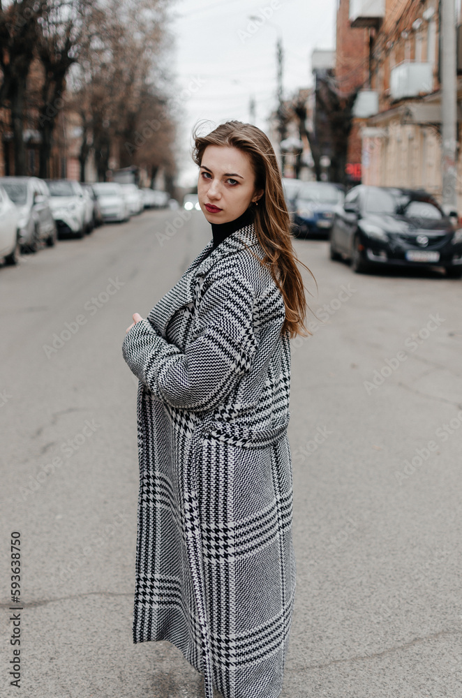 The girl is standing on the street in a gray coat