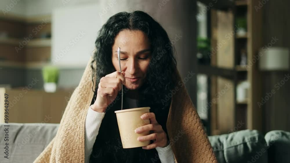 Pretty young hispanic woman looking around to make sure nobody watching and eating ice cream with great pleasure sitting under the blanket at home Break the diet or tasty sweet concept Pretty young hispanic woman looking around to make sure nobody watching and eating ice cream with great pleasure sitting under the blanket at home Break the diet or tasty sweet concept