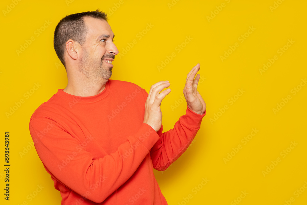 Bearded hispanic man in his 40s wearing a red jumper standing to the side using his hands for protection totally embarrassed and embarrassed. Isolated on yellow background. Bearded hispanic man in his 40s wearing a red jumper standing to the side using his hands for protection totally embarrassed and embarrassed. Isolated on yellow background.