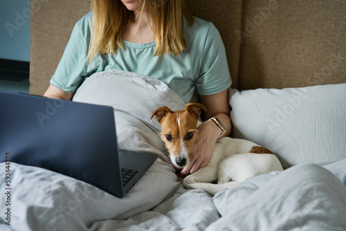 Canvas Print Woman with cute dog relaxing in bed at morning and use laptop