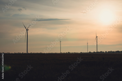 Silhouette of windmills with rotor blades generating alternative form of energy. Producing of renewable source of energy on evening windfarm