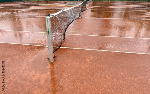 Wet clay tennis court with puddles during the rain. Outdoor tennis season. Spring rain on courts. All practices and match are cancelled! ccourts © Tetiana