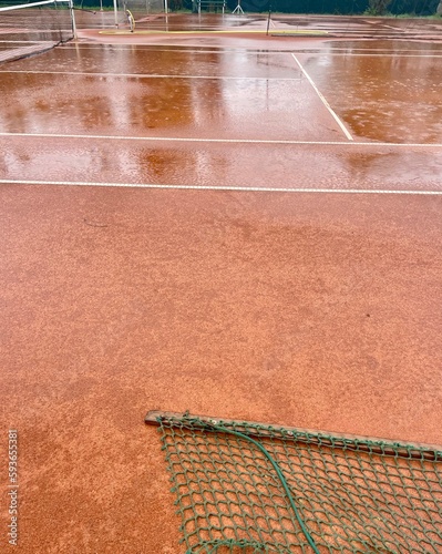 Wet clay tennis court with puddles during the rain. Outdoor tennis season. Spring rain on courts. All practices and match are cancelled! ccourts