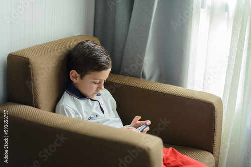 Child sitting in an armchair playing with a smartphone.