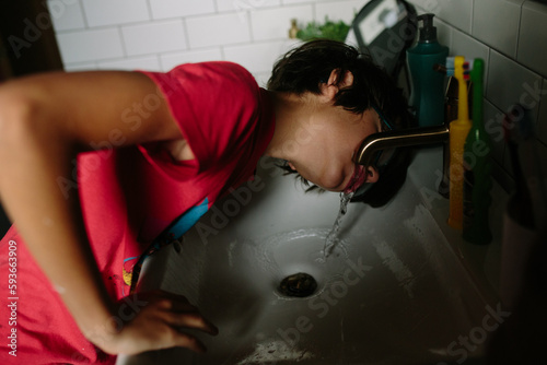 Boy drinks from sink faucet