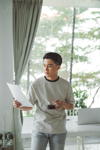 Cheerful young man standing at office, looking at statistical data 
