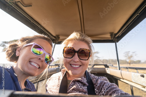 Two women on safari take a selfie out of the rooftop vehicle, in Kenya, Africa