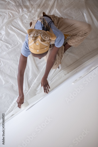 Black painter attaching tape over baseboard