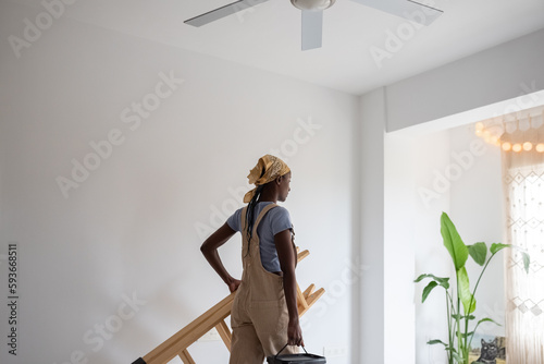 Black woman carrying ladder and paint