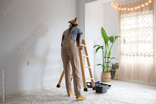 Black painter putting ladder near wall
