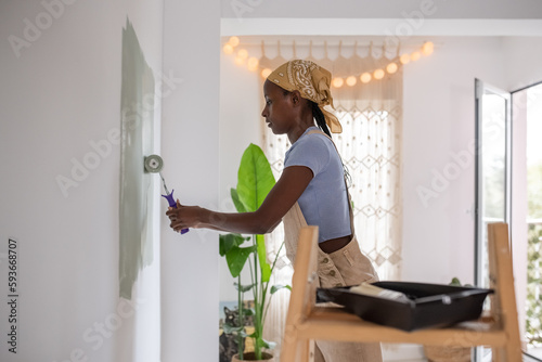 Focused black woman painting wall