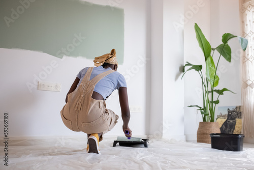Black painter sitting on haunches near unfinished wall