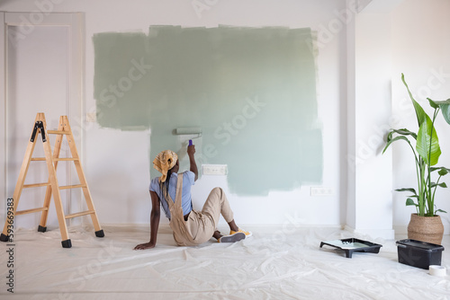 Black woman sitting on floor and painting wall