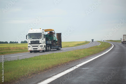 White semi-trailer truck trawl transports oversized machinery on the highway in rainy weather, industry. Copy space for text