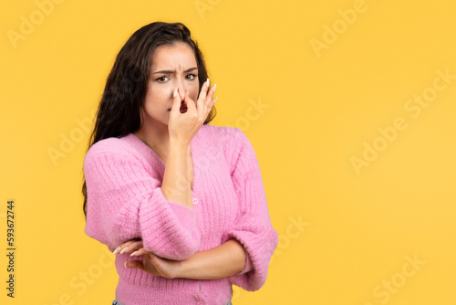 Sad unhappy millennial middle eastern female covering nose with hand  suffering from bad smell