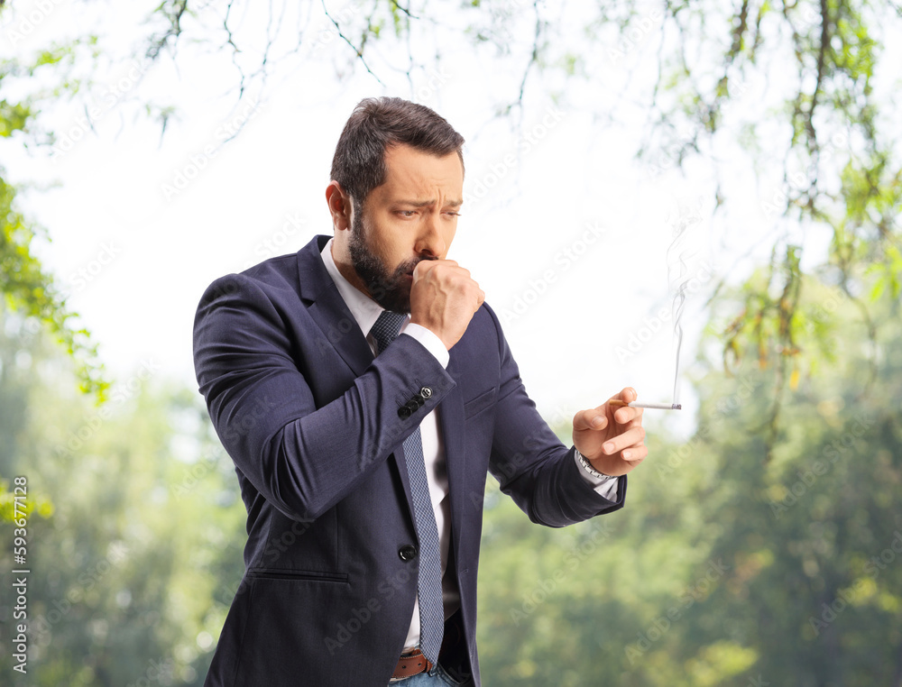 Man smoking and coughing outdoors in a park Man smoking and coughing outdoors in a park