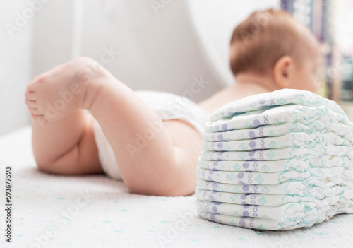 The legs of a baby in a diaper against the background of a stack of children's comfortable diapers, close-up